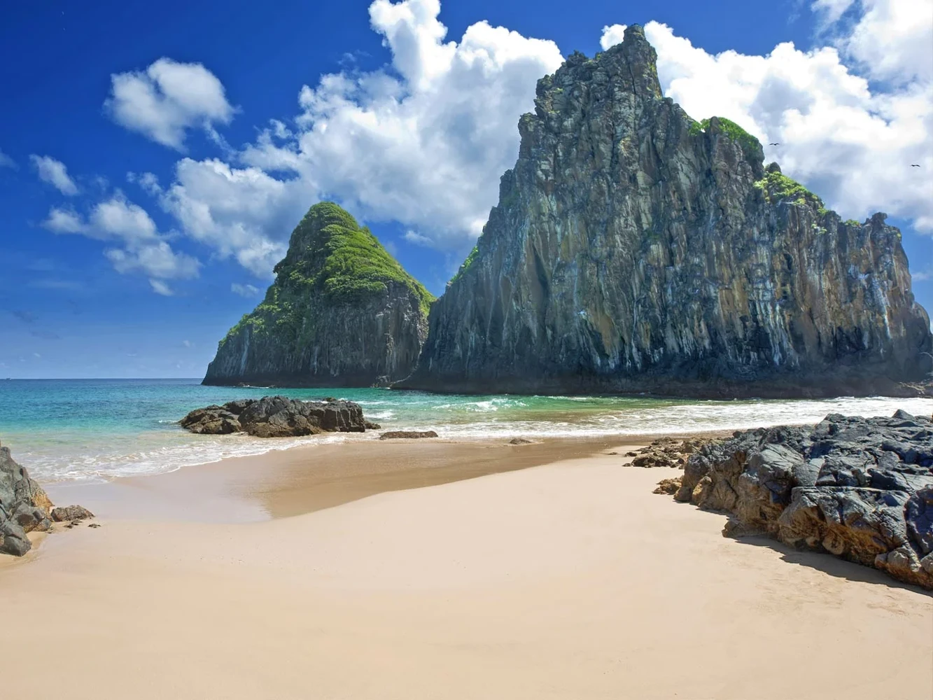 Praia de areia clara junto às formações rochosas de Noronha